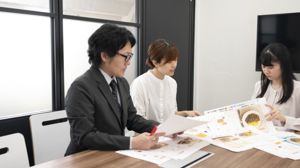 打ち合わせで誌面の色校やデザイン見本を確認する編集スタッフ